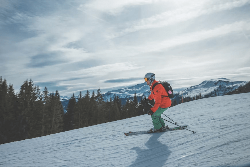 skier skiing down a slope with mountains and trees in the background